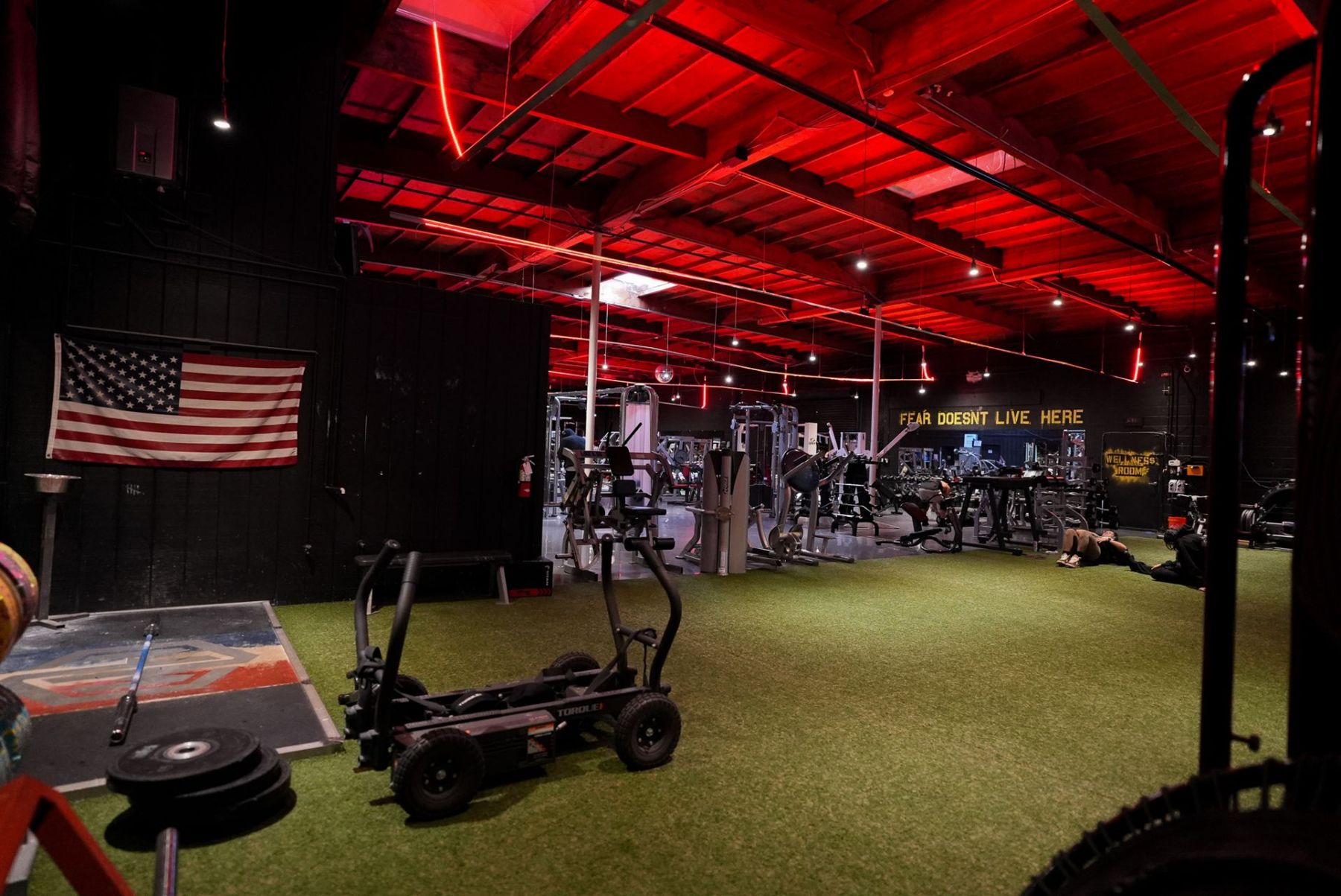 The War House Gyms training floor under red light, with a sled, turf and machines